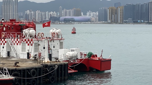 Egret on red fireboat flying a Hong Kong flag. Tall buildings in background.